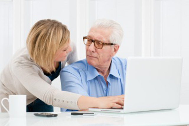 Image of older man at laptop being assisted by younger woman
